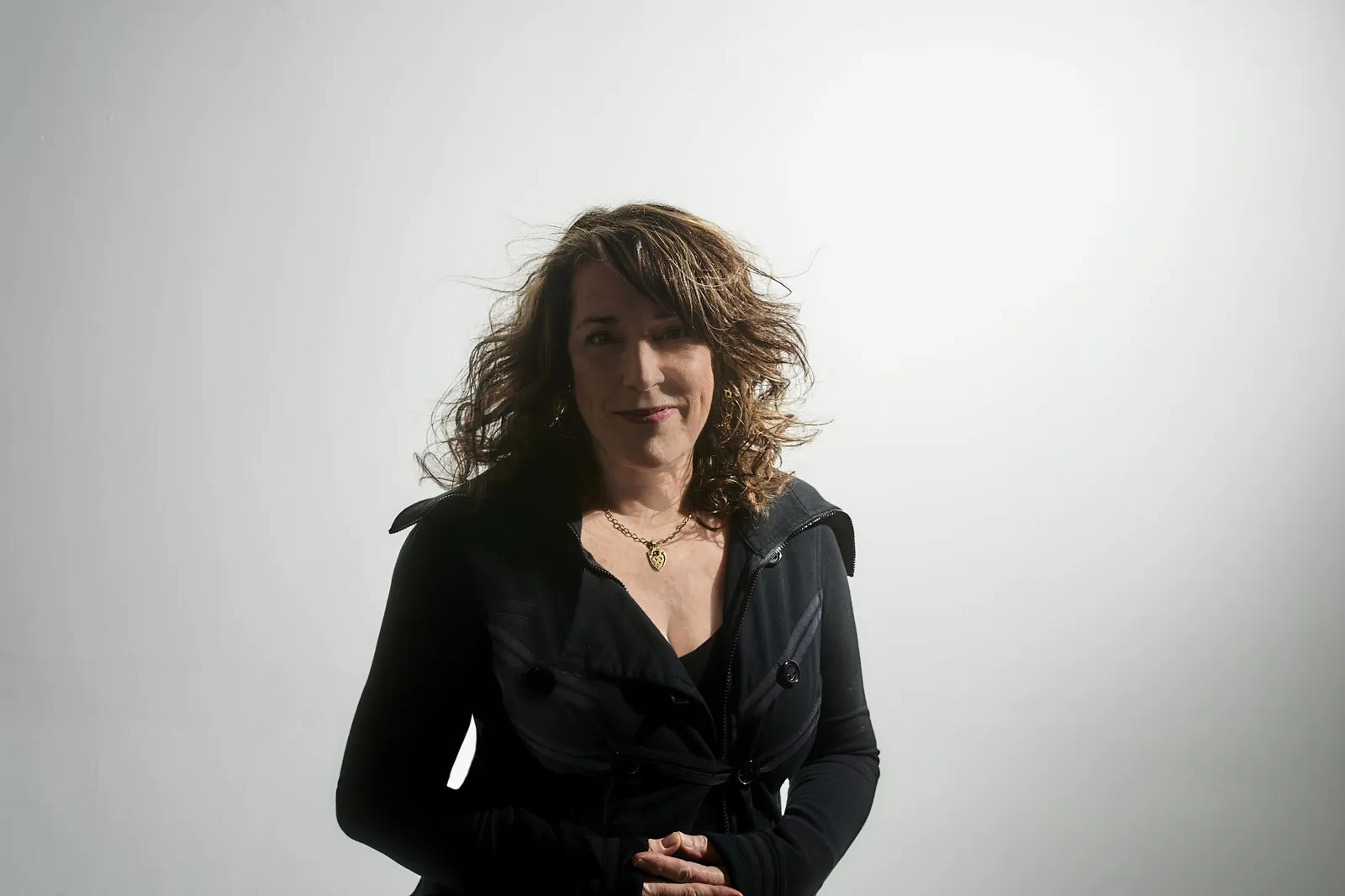 Beth Nielsen Chapman in a dark coat against a plain white backdrop, her hair lifted by a breeze
