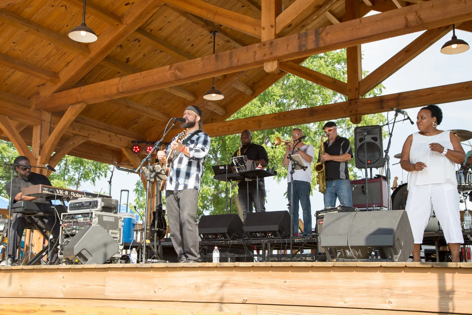 Miller & the Other Sinners playing under a timber pavilion roof, guitar, keys, horns and a singer