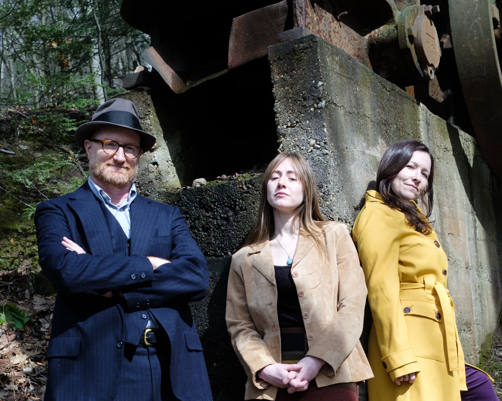 Low Lily's three members standing in front of an old concrete and iron machine in the woods