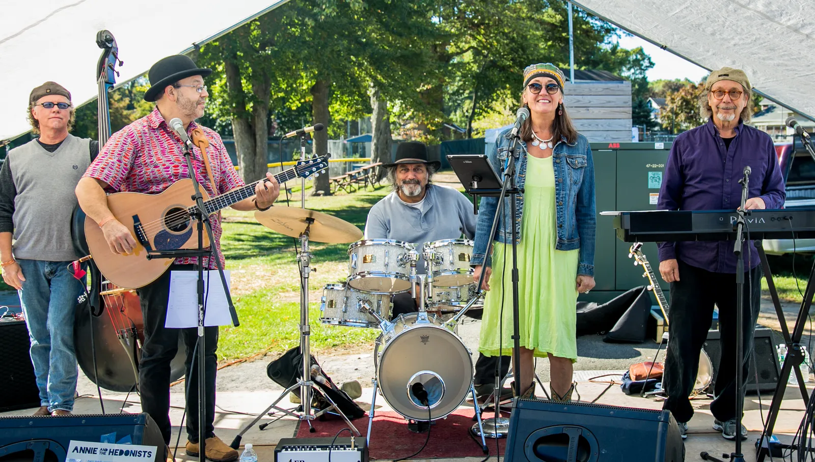 Annie & The Hedonists playing an outdoor stage, five musicians with guitar, drums, keys and upright bass