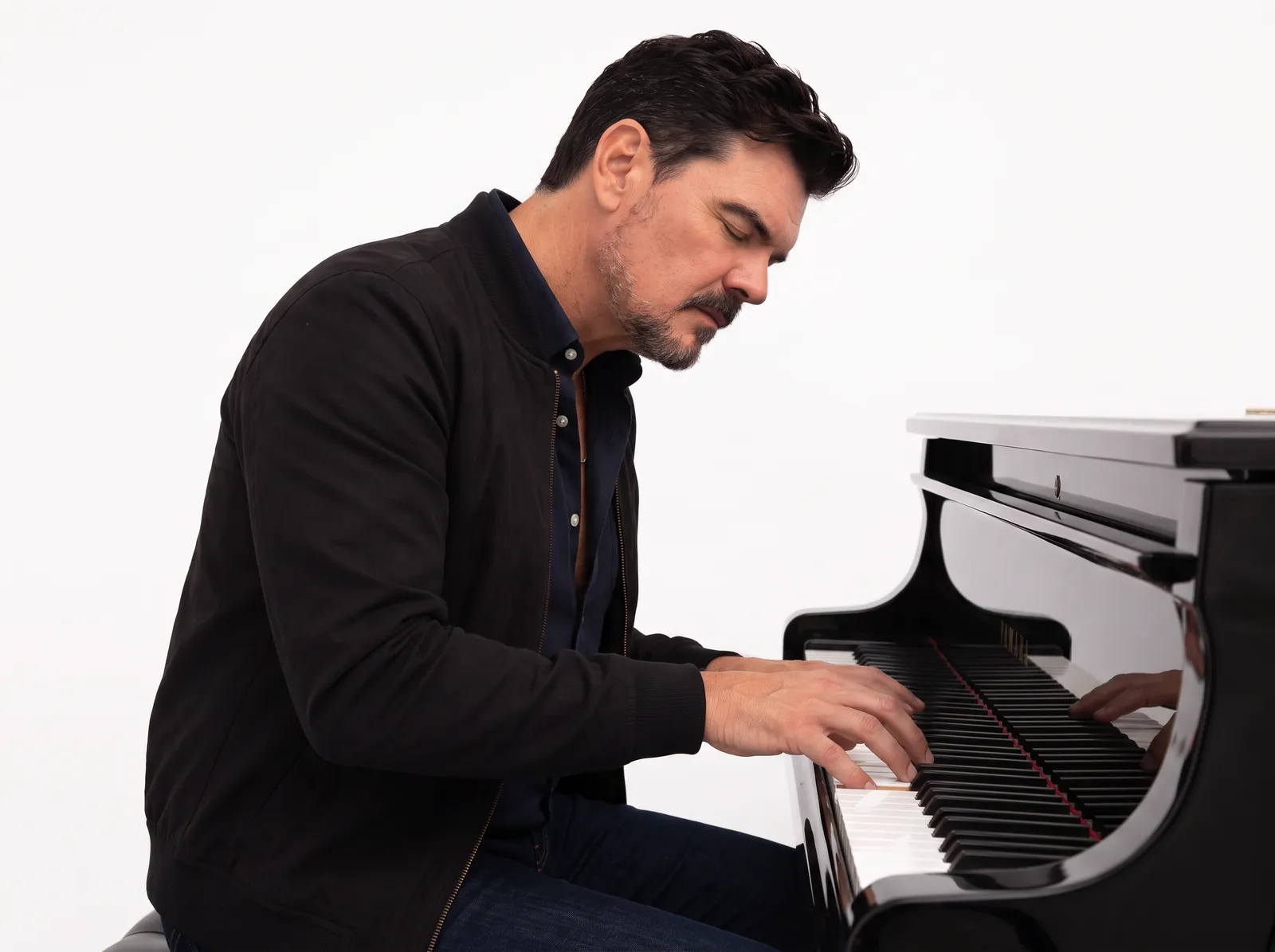 Tom Chick playing a black grand piano against a white backdrop