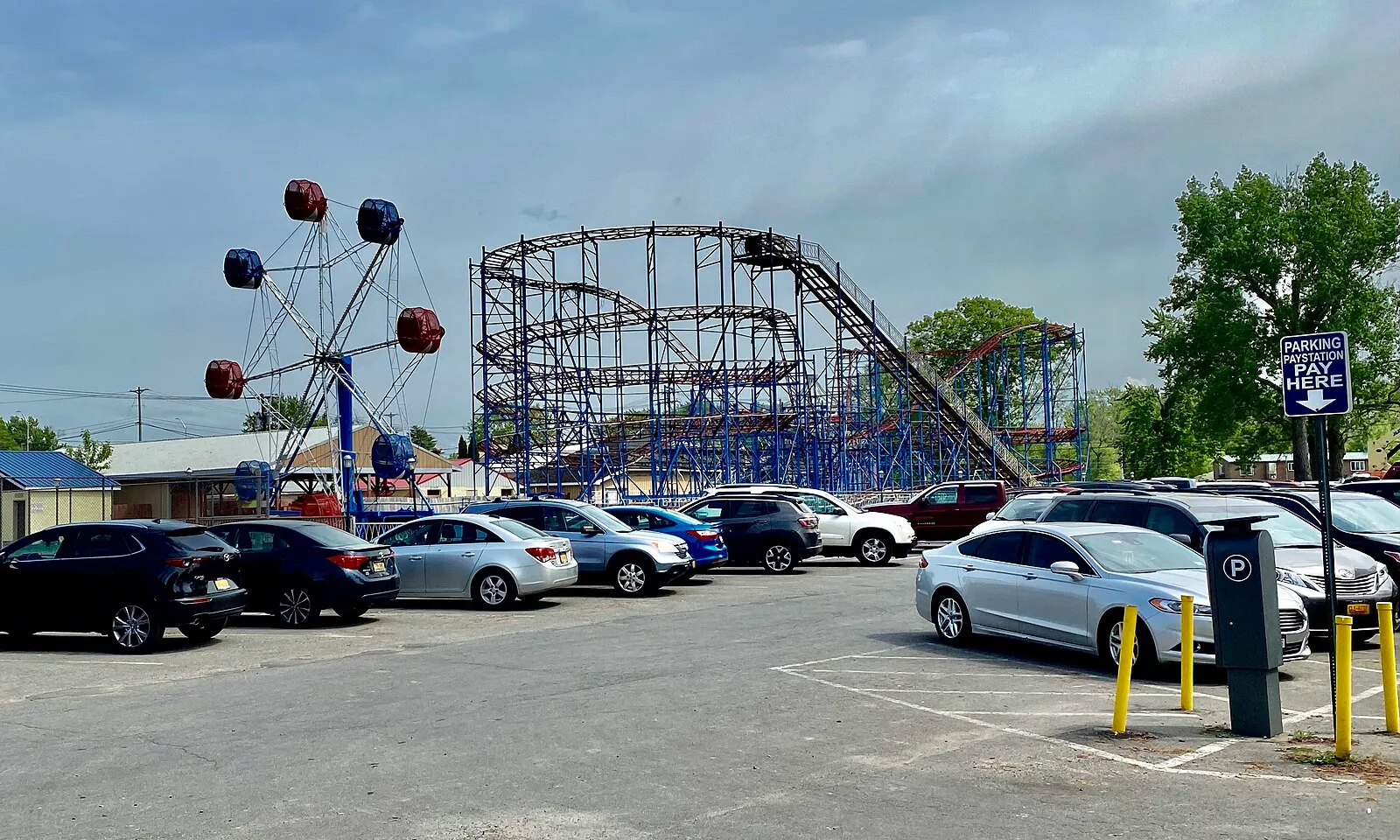 The roller coaster and Ferris wheel of Sylvan Beach Amusement Park above a parking lot on a May afternoon