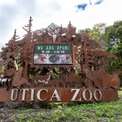 The Utica Zoo's cut-metal entrance sign, with the zoo's hours board set into it