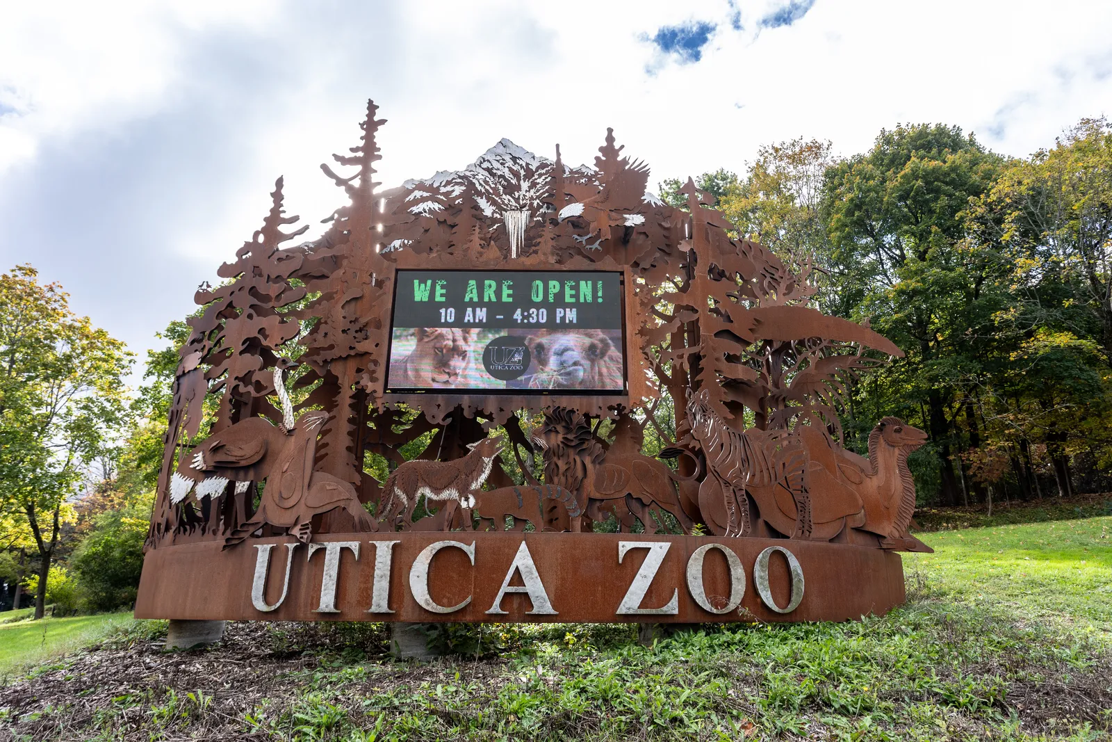 The Utica Zoo's cut-metal entrance sign, with the zoo's hours board set into it